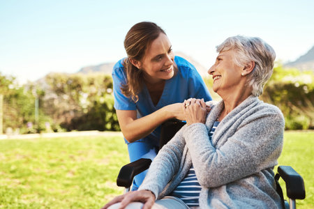Une soignante échange un sourire avec une résidente assise dans un fauteuil roulant, en extérieur.